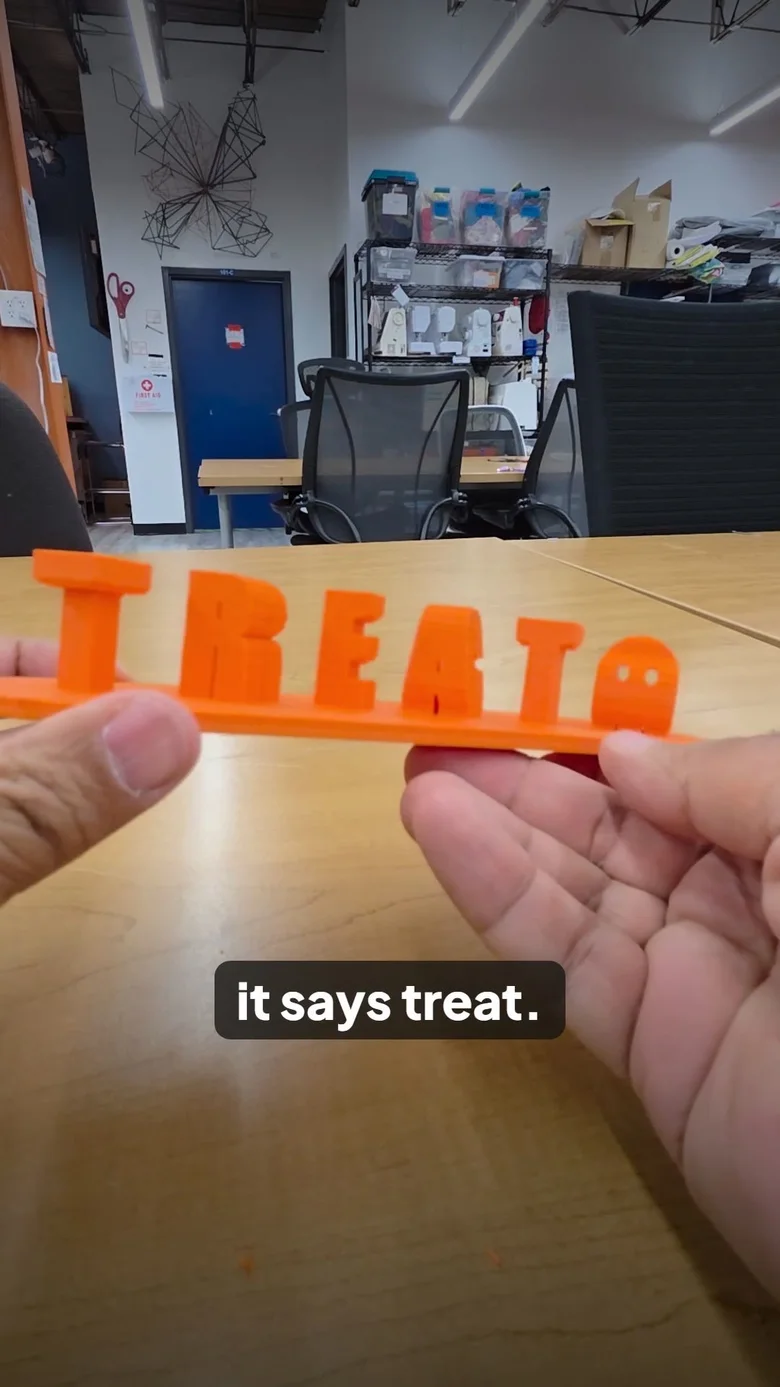 A vertical frame: an orange 3D print that reads TREAT from the side, captioned